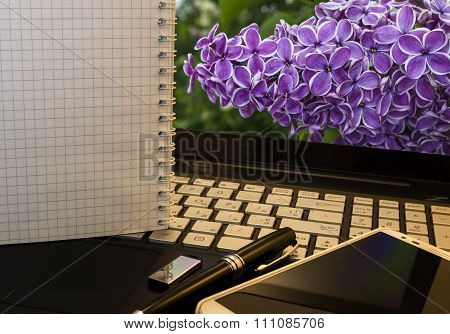 Office Workplace With Notebook, Smart Phone, Pen, Flash Drive And Wordpad With Violet Flowers Backgr