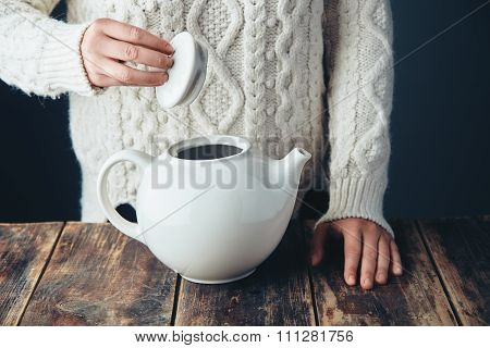 Woman In Warm Sweater Holds Cap Of Big White Teapot In Hands