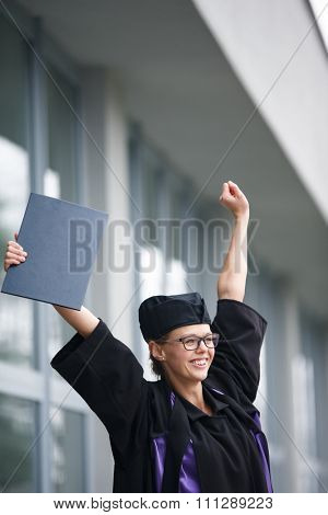 Pretty, young woman celebrating joyfully her graduation - cheking her diploma, happy/impressed with the title she received (color toned image; shallow DOF)