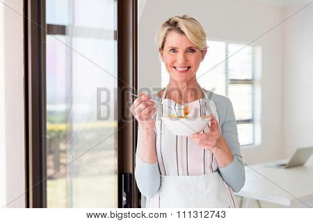 happy mid age woman eating fruit salad at home