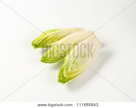 halved heads of fresh belgian endive on white background