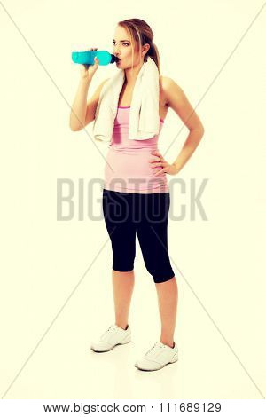 Attractive woman in fitness clothes drinking isotonic drink.