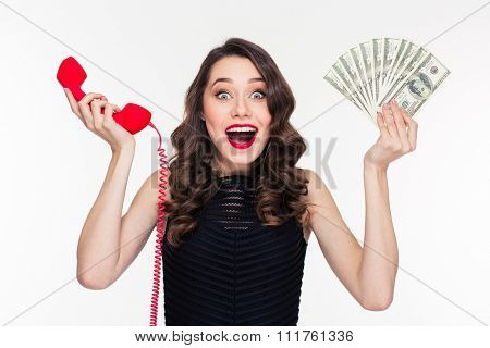 Beautiful excited happy young woman in retro style holding money and telephone receiver over white background