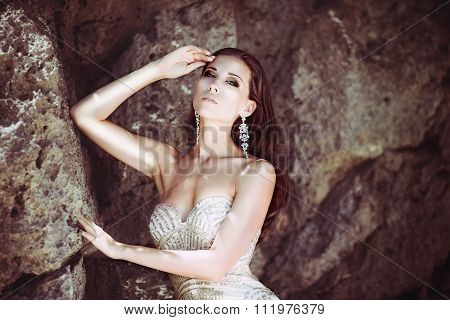 Young beautiful girl in gold dress on the rock of a tropical island. Summer vacation concept.