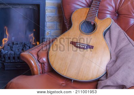 Relaxing winter hobbies. Acoustic guitar on armchair by the fire. Learning a musical instrument in the comfort of home.