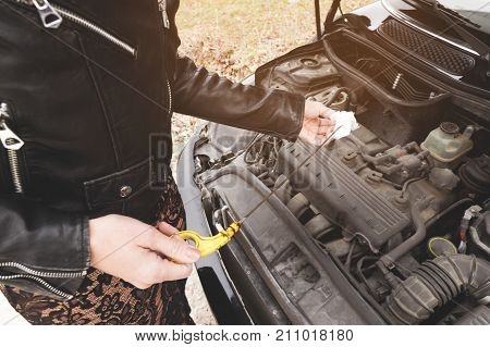 Close-up of the hands The blond girl opens the hood of her car and checks the engine oil level. The concept of car maintenance by women. The concept of a malfunction of the car and its engine