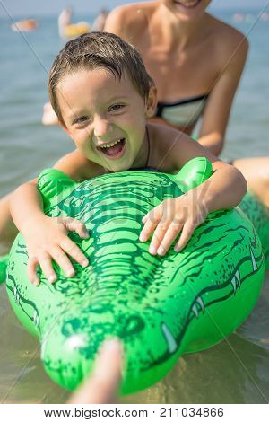 Young mother and smiling baby boy son in green baseball cap playing in the sea in the day time. Positive human emotions feelings joy. Spring and summer holidays.