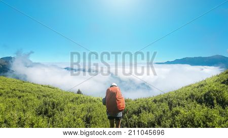 The backpacker is going to see beautiful scenic destination over the clouds with meadow and sky in front of her