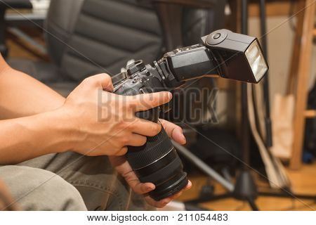 Man holds a DSLR camera with speedlight or flash attached.