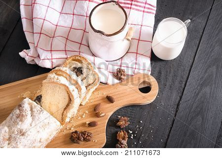Above view over a rustic breakfast with fresh milk and a pound cake sliced on a wooden trencher covered with powdered sugar surrounded by roasted nuts.
