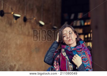 Close up shot of beautiful mixed race young brunette woman looking at the mirror touching hair leaving modern cafe dressing up by the exit. Attractive female student dressed in authentic scarf indoor.