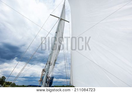 yacht mast with a white sail, the yacht moves with a sail, white sail against a background of cloudy sky