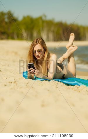 Summertime pleasures enjoying vacation concept. Woman in bikini sunbathing and relaxing on beach using smartphone checking social media and writing sms