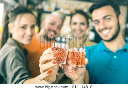 Defocused bokeh of drunk friends toasting cocktails shooters at bar - Food and beverage concept on nightlife birthday party - Focus on hands top cheering red shot glass drinks - Teal and orange filter
