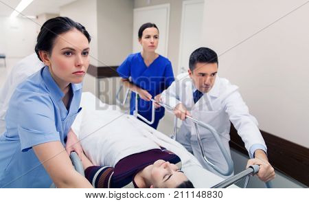 profession, people, health care, reanimation and medicine concept - group of medics or doctors carrying unconscious woman patient on hospital gurney to emergency