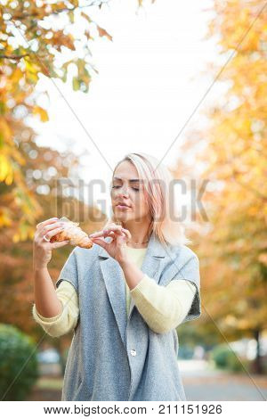 A girl in a gray jacket is holding a croissant in her hand in the park