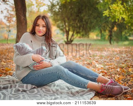A girl in a gray sweater on a coverlet in the fall with a baby
