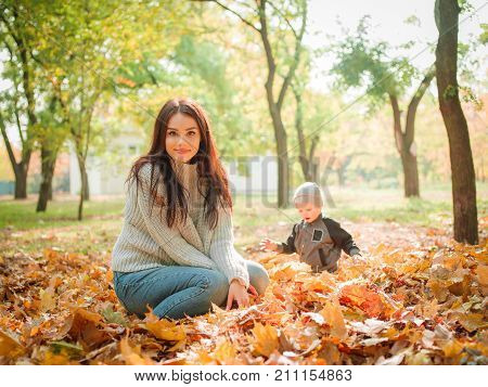 Mom plays with his son in the autumn in the park against the backdrop of fallen leaves