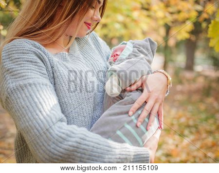 A girl in a gray sweater dark-haired has a son in her arms in the park