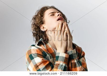 Unleashed emotions and true feelings. Stylish unhappy male teenager with wavy hair throwing back his head closing eyes groaning and touching face feeling desperate or stressed out facing problems