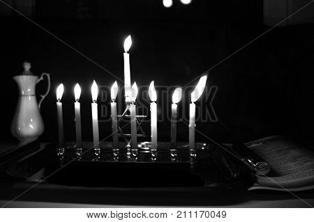Burning Chanukah. The lit Chanukiah. Jewish holiday Hanukkah. Black and white photo. Porcelain jug with oil