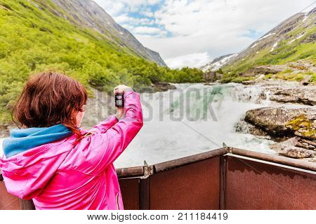 Travel beauty in nature. Tourist woman looking at Videfossen (called Buldrefossen) waterfall taking picture with camera from vieving point Norway Sogn og Fjordane
