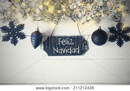 Black Chirstmas Plate With Spanish Text Feliz Navidad Means Merry Christmas. Fir Branch With Fairy Lights On Wooden Background. Black Christmas Decoration Like Balls And Snowflakes.