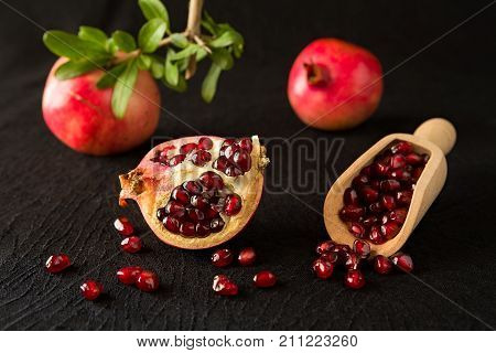 Ripe pomegranate fruits and bailer with seeds inside over a black textured background