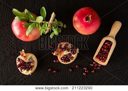 Ripe pomegranate fruits and bailer with seeds inside seen from above over a black textured background