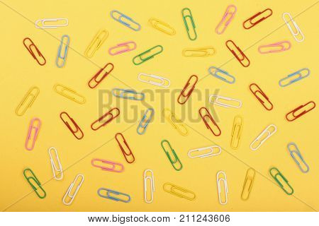 colorful paper clips on yellow background. Top view. Flat lay pattern.