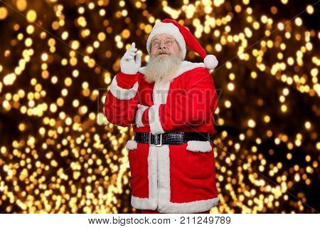 Santa Claus pointing up. Old Santa Claus in red costume and hat raised inex finger and looking upwards. Santa Claus and New Year fairytale.