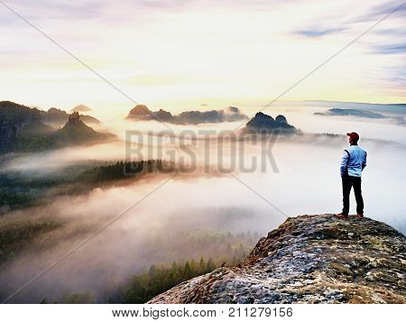Young Hiker In White And Black Siuts  On Cliff Edge Looking To Misty Hilly Valley Bellow, Fall Begin