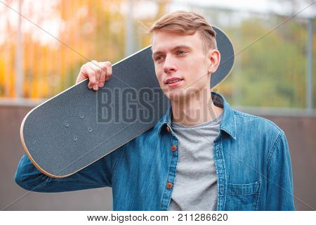 Handsome young boy posing on the camera with skateboard outdoors. Attractive skateboarder having fun in the skatepark. Close-up of man.