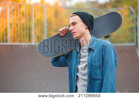 Handsome young boy posing on the camera with skateboard outdoors. Attractive skateboarder having fun in the skatepark. Close-up of man.