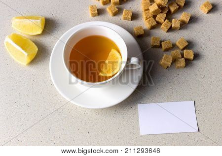 Empty white paper on the table near the white cup of tea with lemon and brown sugar. Top View. Healthy Concept