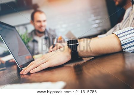 Businessman sitting at wooden table and working on modern laptop on his hand closeup of smart watch on a background group of coworking people developing new startup