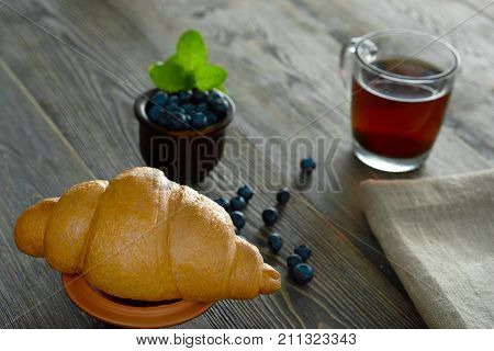 Close up of a delicious freshly baked croissant in front of a cup of tea and a bowl with blueberries copyspace eating food nutrition breakfast healthy natural organic pastry concept.