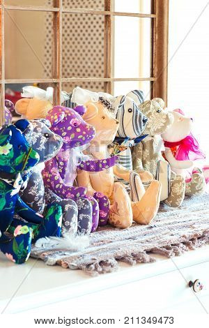 Many tilda textile teddy bear toys sitting in a row in workshop. Indoors.