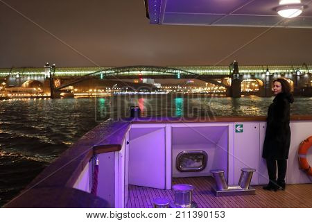 Woman in coat sail on ship in Moscow near Andreevsky bridge at night