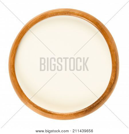 Fresh sweet cream in wooden bowl, a dairy product composed of the higher butterfat layer skimmed from the top of milk before homogenization. Macro food photo close up from above on white background.