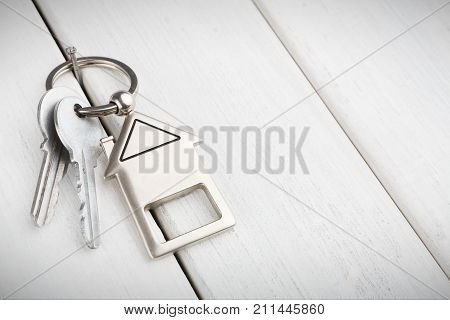 Two steel keys with house shaped trinklet on keyring on white wooden background with copy space. Home key, safety, security, real estate and rent concept
