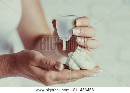 Menstrual cup in female hands. Woman holds flower and silicone hygiene cup, new device for minimize waste and preservation of the environment