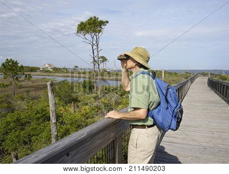 Man with binoculars and backpack on elevated boardwalk at Big Lagoon State Park in Florida