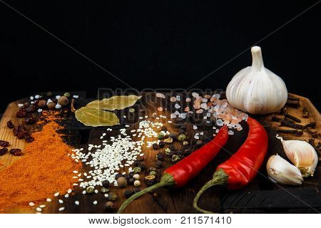 Composition with a cutting board, spices and hot pepper and garlic on a black background. Concept of food, spices, restaurant. Free space for text.
