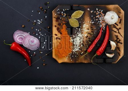 Composition with a cutting board, spices and hot pepper, onion and garlic on a black background. Concept of food, spices, restaurant. Free space for text.