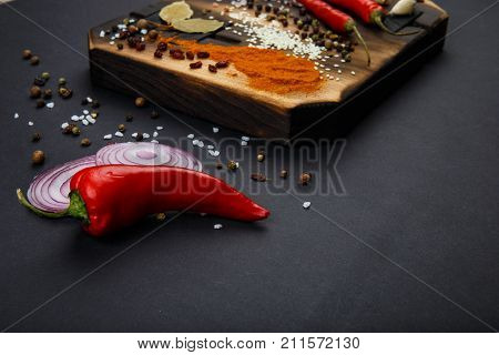Composition with a cutting board, spices and hot pepper, onion and garlic on a black background. Concept of food, spices, restaurant. Free space for text.