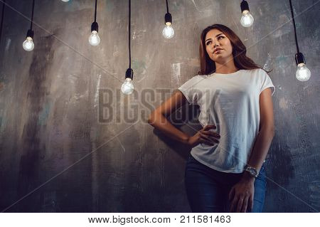Sexy woman in a white T-shirt on a gray background with light bulbs. Mock-up.