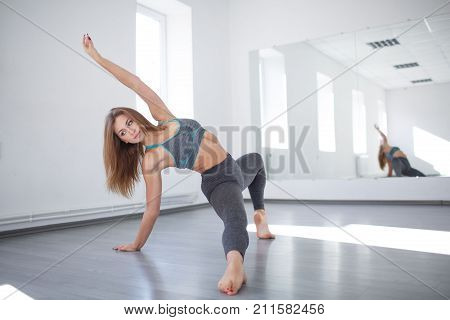 Young attractive, athletic girl, in a gray suit performs dance elements in the studio in front of a mirror. The concept of sport, sports dancing.