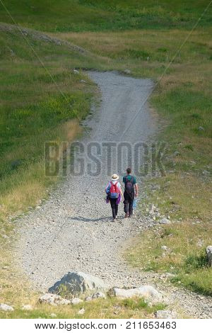 young couple of hikers with backpack walking on stony path, Montenegro
