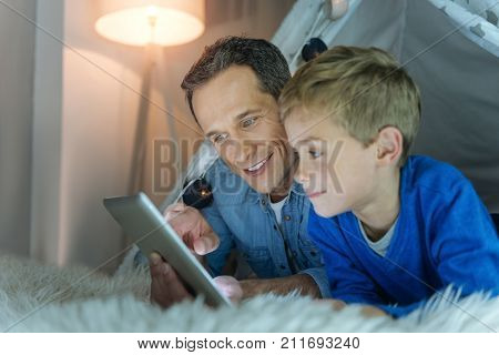 Happy together. Delighted male person keeping smile on his face and bowing head while talking to his son